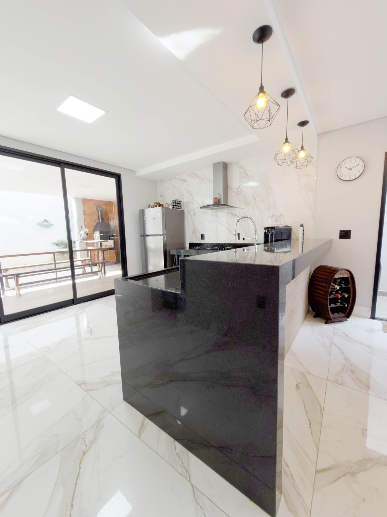 Cozinha com bancada em granito, cooktop, coifa e acesso à área gourmet