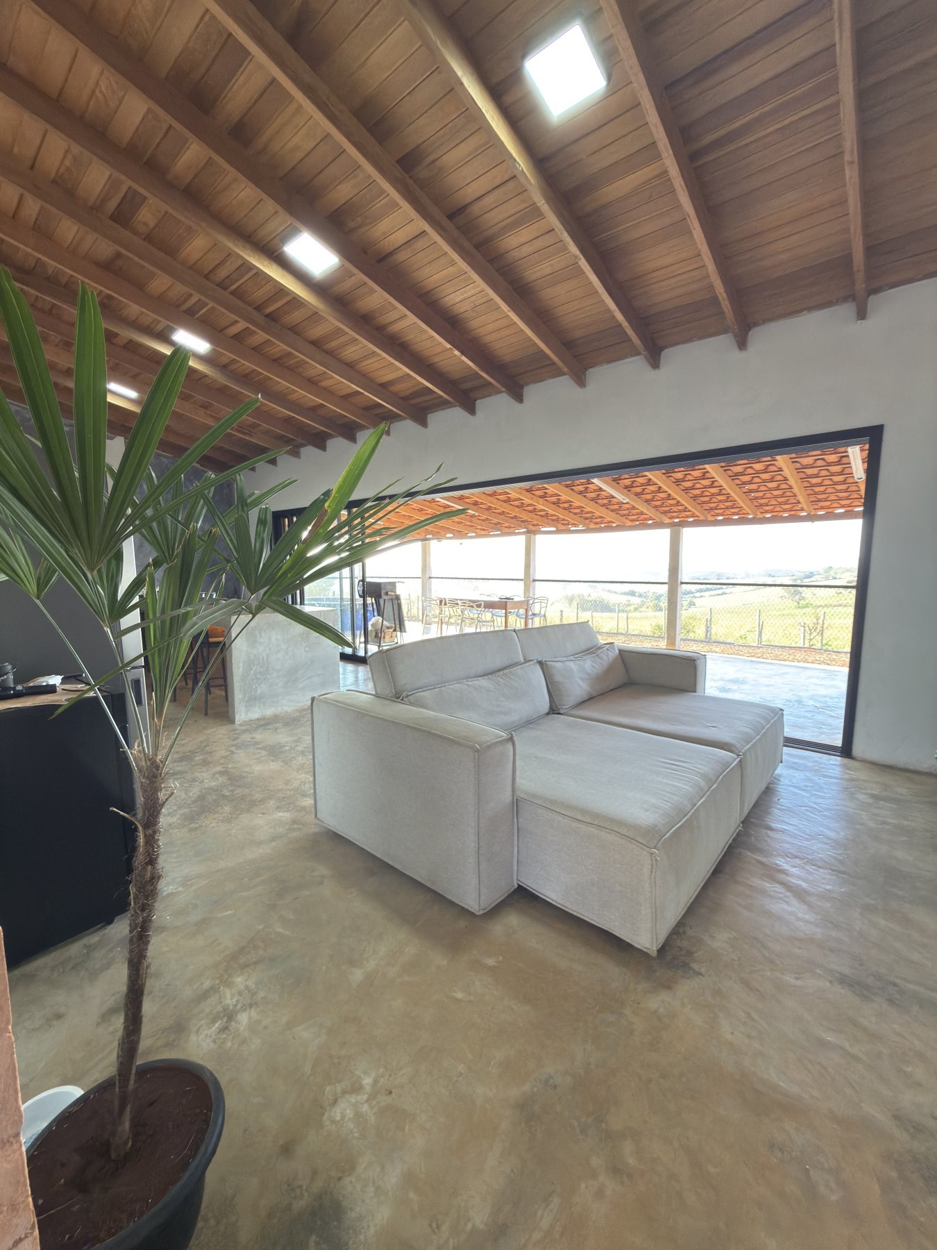 Sala integrada do rancho, com sofá, vegetação e vista para a varanda e o campo