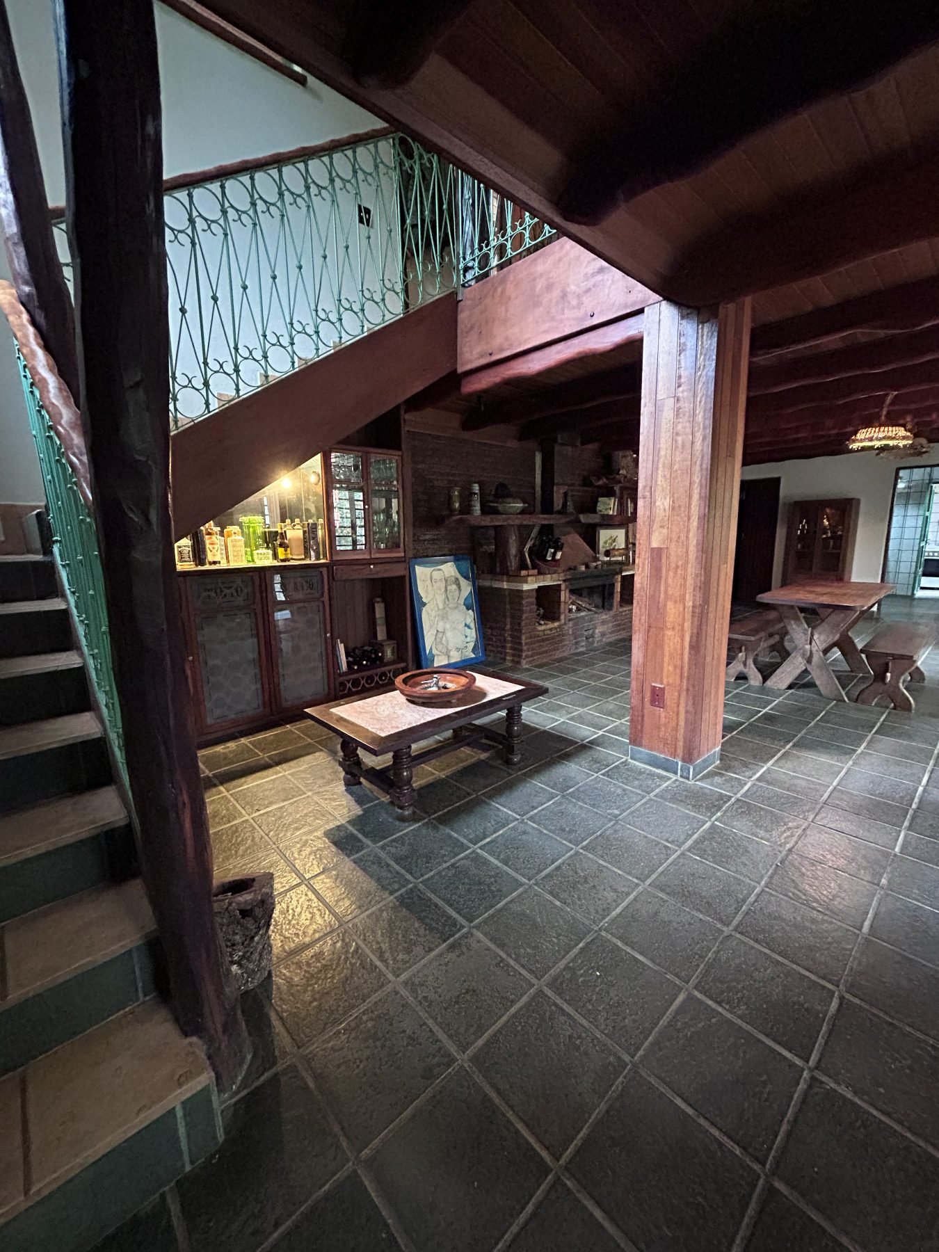 Sala de estar da casa de apoio, com escada, lareira e bar