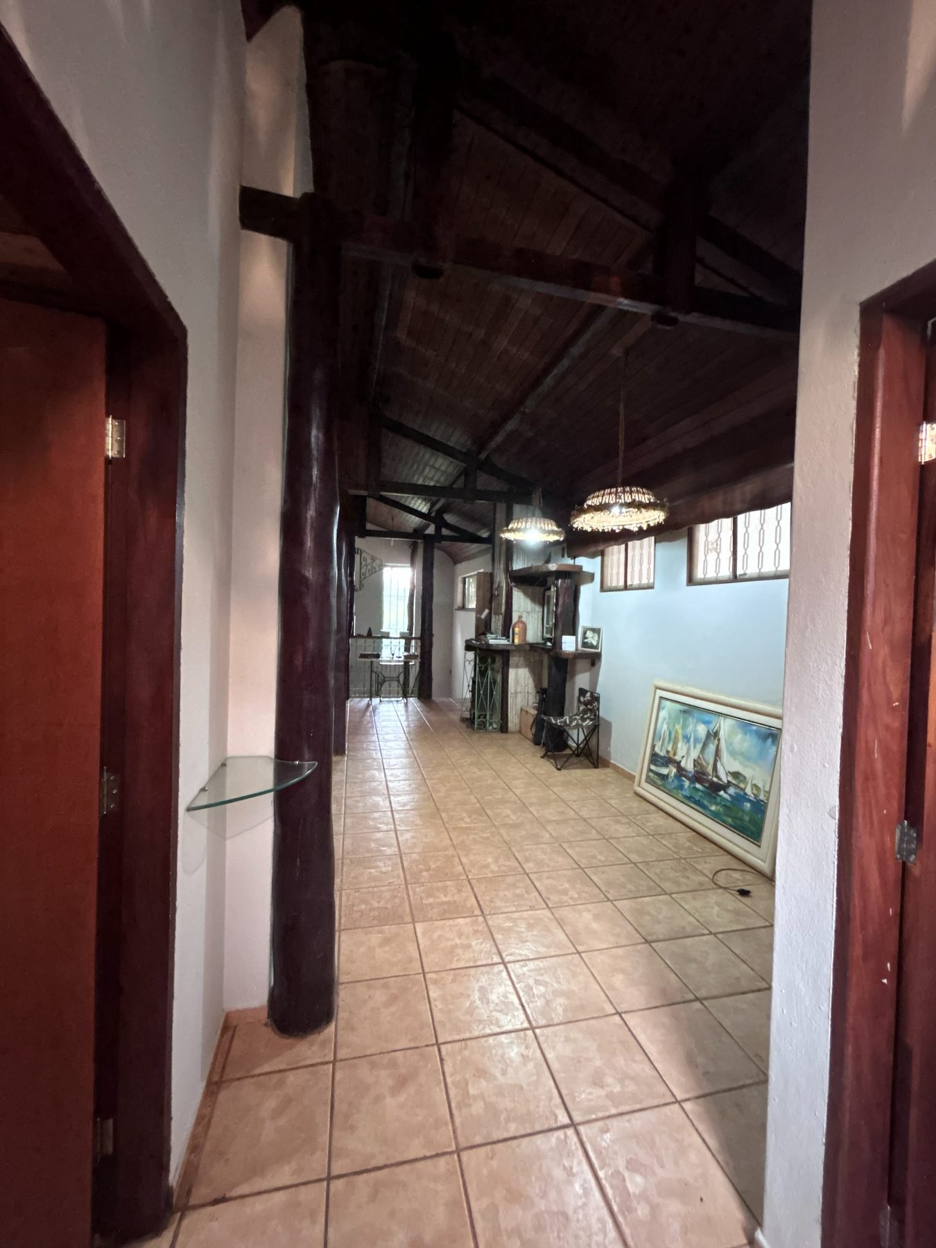 Corredor interno da casa de apoio, com pé-direito alto e vigas de madeira aparentes